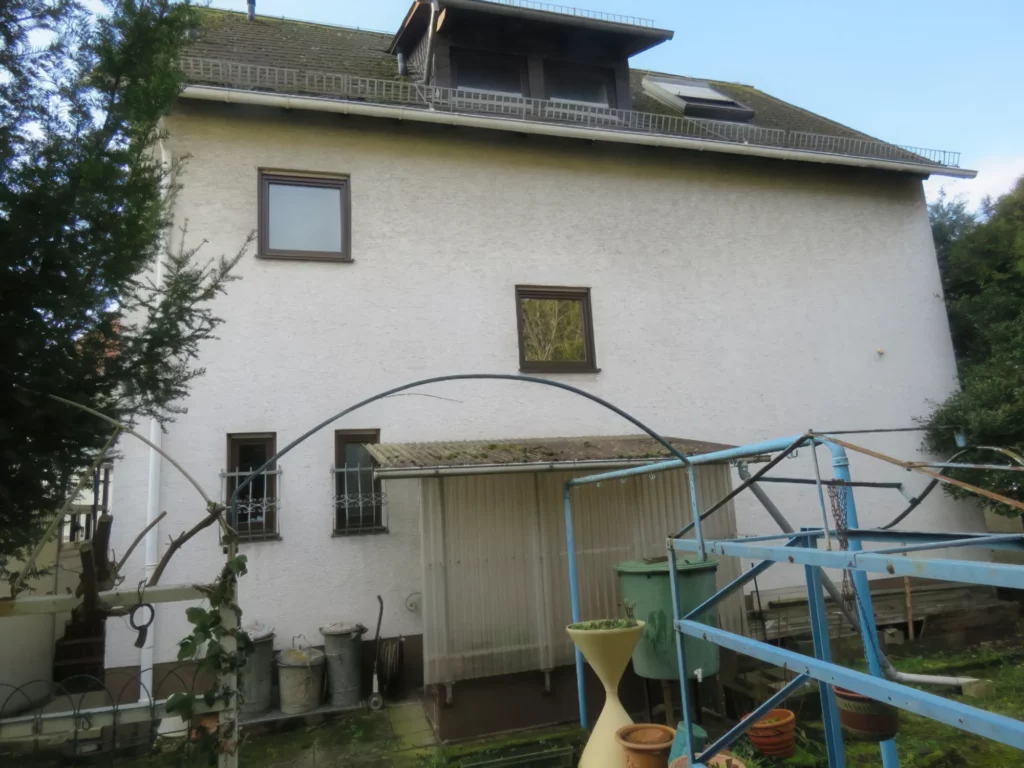 Gartenansicht eines hellen Einfamilienhauses mit Garage und Gartengeräteschuppen.