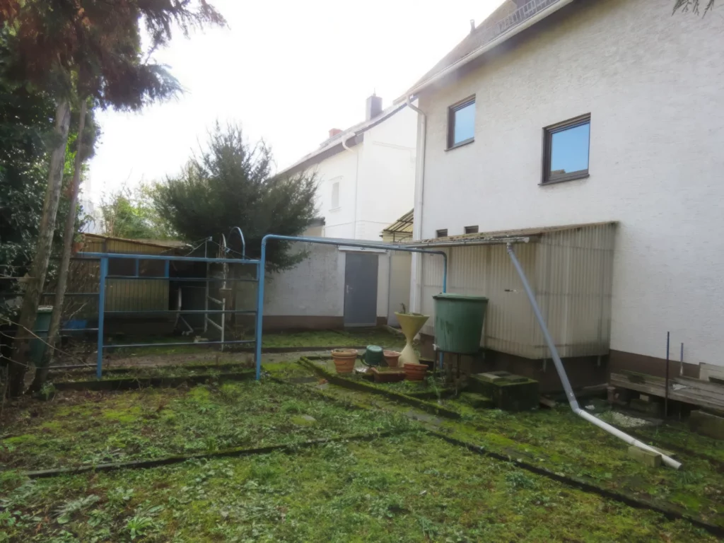 Der Garten eines Einfamilienhauses mit Rasen, Geräteschuppen und Regenwassertonne.