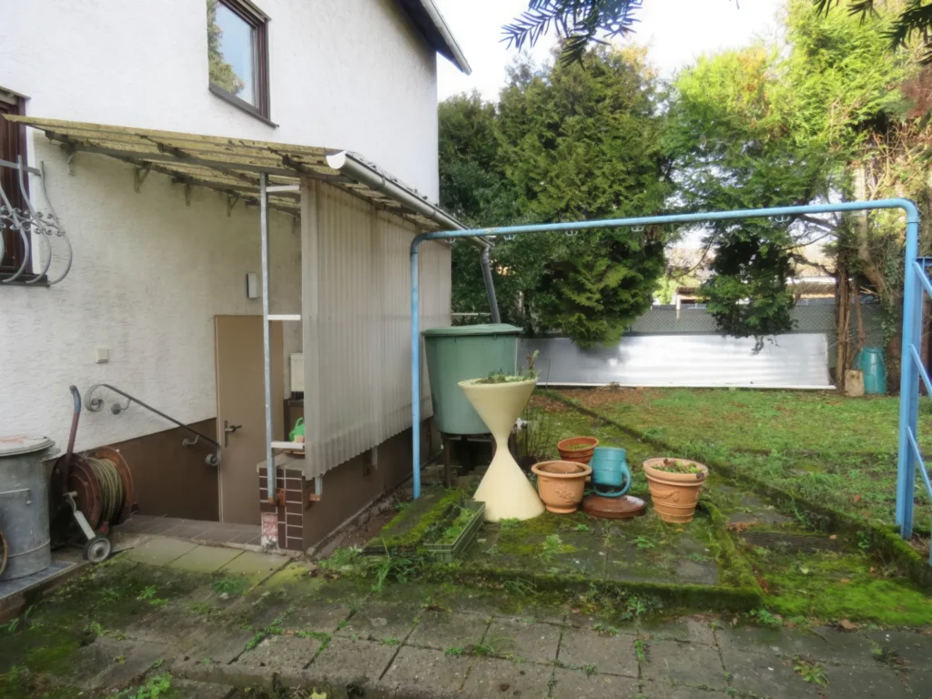 Blick auf den Garten eines Einfamilienhauses mit Garage und Gartengeräten.