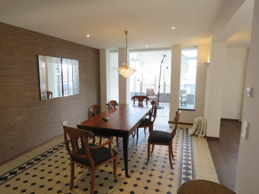 Dining area with a long wooden table, chairs, chandelier, and a view to a balcony in a luxurious Bad Soden apartment.