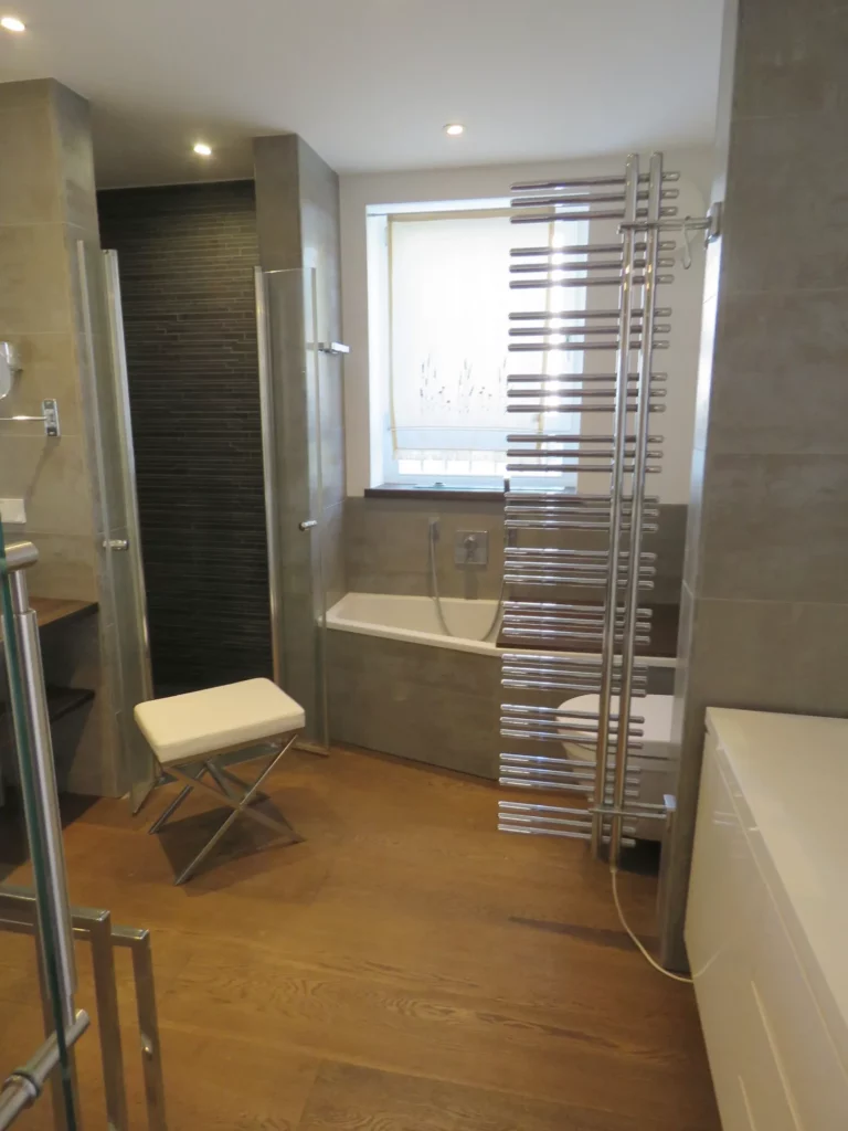 Modernes Badezimmer mit Holzboden, Badewanne, Handtuchwärmer und Hocker in einer Wohnung in Bad Soden.