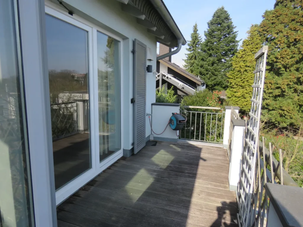 View of the apartment's wooden terrace with sliding glass doors, a shutter, and a view of the trees.